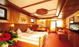 A cozy bedroom with wooden details and a red carpet. There is a large bed, a living area, and plenty of daylight.