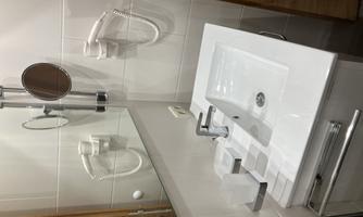 A modern bathroom with a white sink and a large mirror. A hairdryer and an adjustable cosmetic mirror are mounted on the wall.