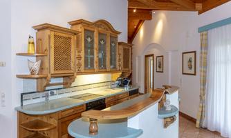 A modern kitchen with wooden shelves and a bright, open space. Bright tiles and large windows ensure plenty of light.