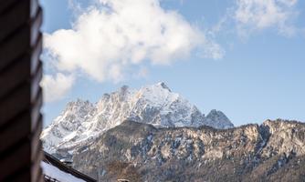 An impressive mountain with a snow-capped peak beneath a clear sky. The surrounding landscape is green and mountainous.