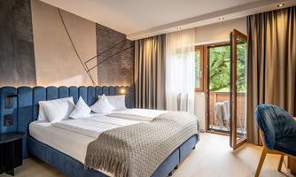 A modern bedroom with a large, blue bed and elegant decoration. The room has large windows that offer a view of nature.
