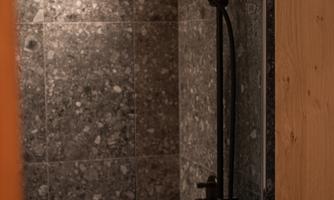 A modern shower with a black shower system and gray stone tiles. The atmosphere is elegant and minimalist.