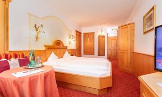 A cozy hotel room with two beds and a table. The wood paneling and the red carpet create a warm atmosphere.