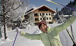 A cheerful person in a snow-covered ski resort. In the background, you can see a cozy hotel and snow-covered trees.