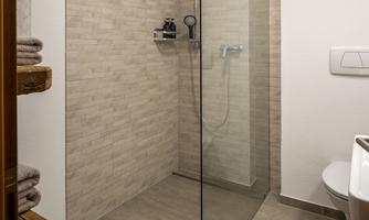 A modern shower with a glass wall in a neutral bathroom. The walls are tiled in light colors and the floor is in neutral tones.