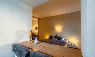 A cozy bedroom with a large bed and warm lighting. The adjoining area is modernly furnished and inviting.