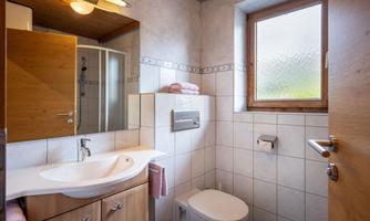 A modern bathroom with wood paneling and bright tiles. It features a sink, a toilet, and a shower.