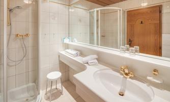 A modern bathroom with a shower and a bathtub. The walls are light-tiled and the room is well-lit.