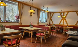 A cozy restaurant with wooden furniture and warm lighting. The tables are set for guests, and there are decorations on the windows.
