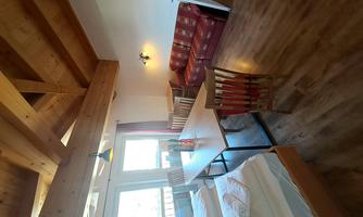 A bright room with a wooden beam ceiling, two single beds, and a dining table. In the background, there is a cozy seating area with a sofa.