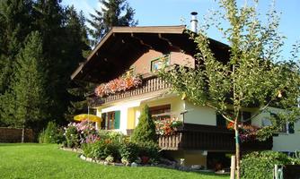A beautiful house surrounded by green meadows and trees. The balcony is adorned with colorful flowers.