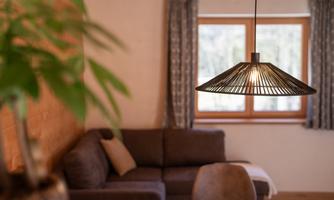 A cozy living room with a modern lamp above a table. In the background, there are windows with curtains and a comfortable sofa visible.