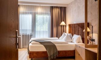 A modern bedroom with a double bed and light curtains. The room is cozy with soft colors and warm lighting.