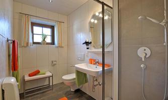 A modern bathroom with a shower, sink, and toilet. The walls are tiled in light colors, and there are colored towels as well as decorative elements.
