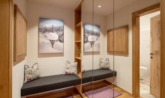 A modern hallway with a wooden shelf and mirror walls. Two cozy seating cushions and pictures of snowy landscapes decorate the space.