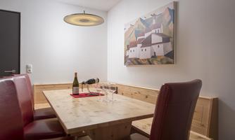 A modernly designed dining area with a wooden table and red chairs. A piece of artwork hangs on the wall, and on the table are a wine bottle and glasses.