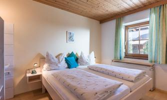 A cozy bedroom with two beds and a wooden ceiling. Gentle light falls through the window onto the decoration.