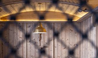 A cozy room with a wooden paneled wall and a golden pendant lamp. In the foreground, a grid is visible, limiting the view of the table with drinks.