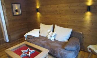 A cozy living room with a brown couch and white cushions. On the wall are wooden paneling and two wall lamps.