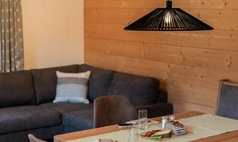 A cozy dining area with a wooden table and modern chairs. In the background, a brown sofa is situated against a wooden wall.