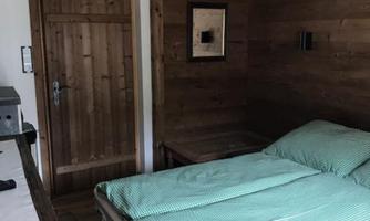A cozy bedroom with a wooden interior. The bed has green bedding and a wooden door leads outside.