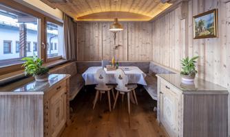 A cozy dining area with paneled wooden walls and a round table. Plants and soft lighting create an inviting atmosphere.