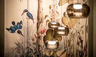 A beautiful mural featuring hummingbirds and plants. In the foreground, modern, shiny lamps hang.