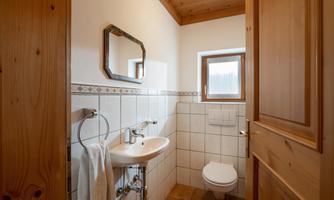 A modern bathroom with wooden ceilings and white walls. There is a sink, a toilet, and a small window.