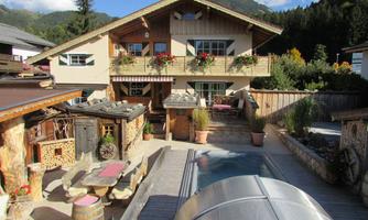 A beautiful, rustic house with flowers at the windows. The outdoor area has cozy seating and a pool.
