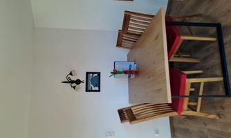 A bright dining room with a wooden table and chairs in warm colors. A small picture hangs on the wall, and there is a mirror that makes the room appear larger.