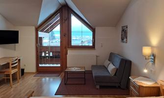 A cozy room with a sleeping area and a living area. Large windows offer a view of the surroundings.
