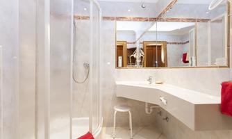 A modern bathroom with a shower and a curved sink. Red towels and a stool give the space an inviting touch.