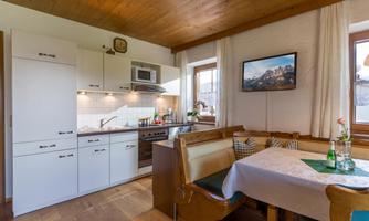 A cozy kitchen with wooden elements and modern amenities. A dining table with comfortable seating and windows that provide plenty of light.