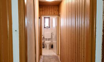 A narrow hallway with wooden walls and a carpeted floor. At the end of the hallway, a bathroom can be seen.