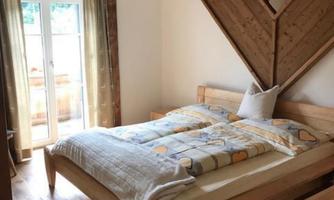 A cozy bedroom with a wooden bed and a warm blanket.  
Large windows let in a lot of daylight.
