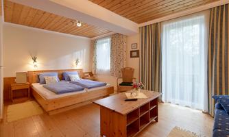 A cozy bedroom with a double bed and wooden decor. The windows let in plenty of daylight, and the room feels inviting and bright.