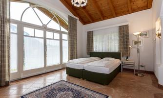A cozy bedroom with a double bed and a large window. The room has a wooden ceiling and a carpet on the floor.