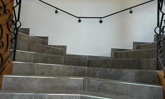 An elegant staircase with gray tiles and a curved handrail. Stylish lights are mounted on the wall in the background.