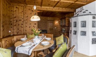 A cozy dining area with wooden paneling. The table is set and a traditional stove can be seen in the corner.