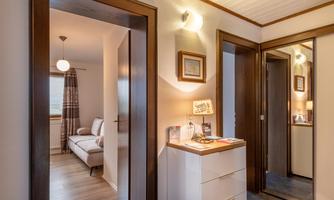 A bright hallway with modern wooden frames and a mirror. On the left side, there is a cozy room with a couch.