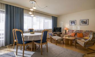 A bright and inviting living room with a dining table and comfortable seating options. Large windows provide plenty of daylight and a cozy atmosphere.