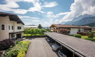 A quiet residential area with several buildings and green spaces. In the background, there are mountains and a clear blue sky.