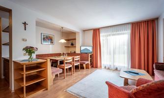 A cozy living room with a dining area and wooden furniture. Large windows provide plenty of natural light and a friendly atmosphere.