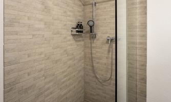 A modern shower with bright tiles and a clear glass shower curtain. Care products are on the wall in elegant bottles.
