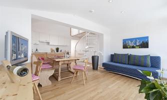 A bright, modern apartment with an open living area. The space is furnished with a dining table, a couch, and an elegant spiral staircase.