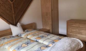 A cozy bedroom with a wooden bed and a colorful bedspread. The walls are made of wood, and there is a wooden wardrobe and a chest of drawers.