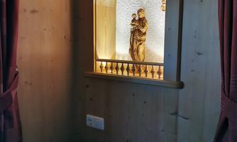A beautiful, illuminated area with a statue in a niche. The wall is made of wood and is surrounded by a red curtain.