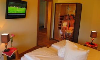 A cozy bedroom with a large bed, a television, and modern lamps. In the background, a sauna is visible, providing relaxation.