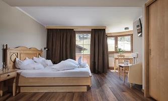 A bright and cozy bedroom with a double bed and wooden furniture. Large windows offer a view outside and the furniture is simple and functional.