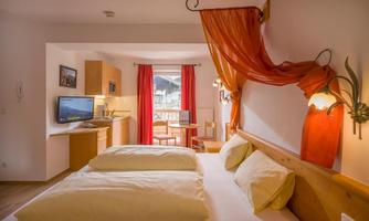A cozy room with a double bed and bright pillows. There is a small table, a television, and a balcony with a view.
